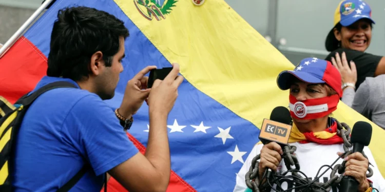 ARCHIVO - Un hombre toma una fotografía de una mujer que, mientras sostiene micrófonos, lleva una mordaza y una cadena. Fue durante una manifestación para conmemorar el día Mundial de la Libertad de Prensa en Caracas, Venezuela, el 3 de mayo de 2016