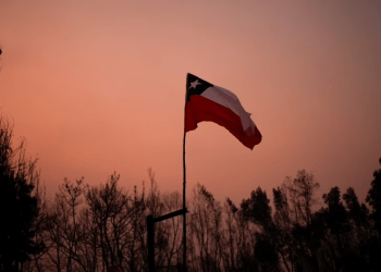 Una bandera chilena colocada en medio de árboles carbonizados bajo un cielo rojo causado por incendios forestales en Santa Juana, Chile, el 5 de febrero de 2023.