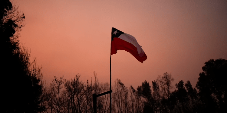 Una bandera chilena colocada en medio de árboles carbonizados bajo un cielo rojo causado por incendios forestales en Santa Juana, Chile, el 5 de febrero de 2023.