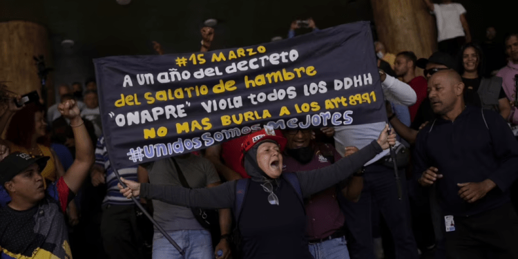 Un manifestante sostiene un cartel que exige mejores salarios mientras los partidarios del gobierno se paran detrás en un intento de que los manifestantes abandonen el Ministerio de Trabajo en Caracas, Venezuela, el miércoles 15 de marzo de 2023. (Foto AP/Matías Delacroix)
