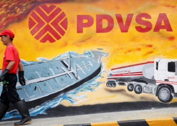 Un empleado de una estación de servicio de Caracas pasa frente a un mural con el logo de la estatal petrolera PDVSA, en agosto de 2014.