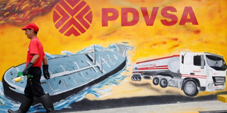 Un empleado de una estación de servicio de Caracas pasa frente a un mural con el logo de la estatal petrolera PDVSA, en agosto de 2014.
