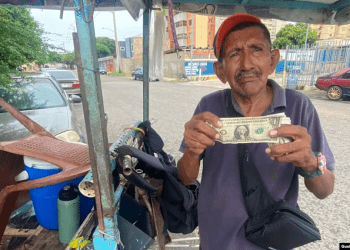 Un vendedor ambulante de golosinas y cigarros muestra un billete de un dólar estadounidense en Maracaibo, Venezuela.