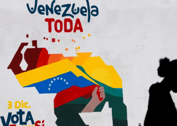 Una mujer vende frutas frente a un mural con el mapa de Venezuela donde se promueve la participación pro oficialista en el referendo consultivo del domingo, en Caracas, el 29 de noviembre de 2023.