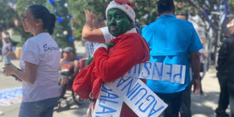 Trabajadores activos y jubilados de Venezuela, uno de ellos disfrazado del personaje el Grinch, se manifiestan por mejores salarios, el pago completo de aguinaldos y pensiones más "dignas" en Caracas, el 9 de noviembre de 2023.