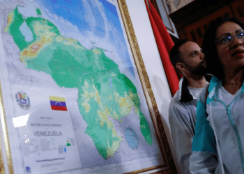 Dos personas conversan cerca de un mapa enmarcado de Venezuela, promovido por el gobierno de Nicolás Maduro para anexar un nuevo estado, el Guayana Esequiba, en Caracas, el 8 de diciembre de 2023.