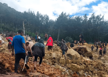 En esta imagen proporcionada por la Organización Internacional para las Migraciones, un grupo de personas cruza un área afectada por un deslave para llevar a la otra área de la aldea de Yambali, en Papúa Nueva Guinea, el viernes 24 de mayo de 2024.