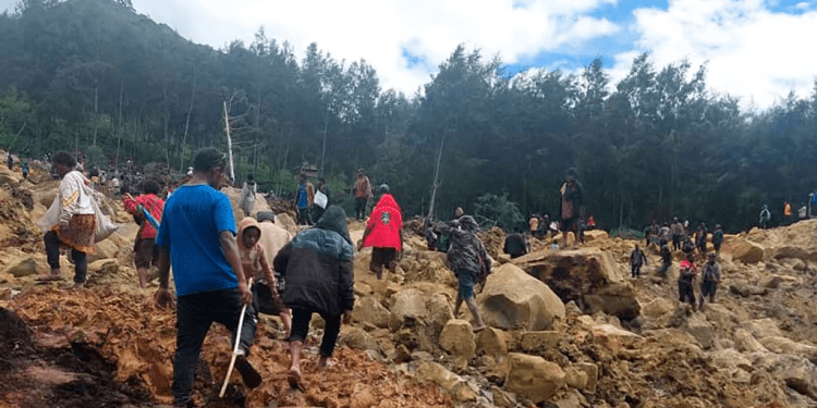 En esta imagen proporcionada por la Organización Internacional para las Migraciones, un grupo de personas cruza un área afectada por un deslave para llevar a la otra área de la aldea de Yambali, en Papúa Nueva Guinea, el viernes 24 de mayo de 2024.