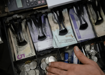 Un vendedor cuenta bolívares venezolanos y billetes de dólares estadounidenses para entregar el cambio a un cliente en un mercado público en Caracas, Venezuela, el martes 18 de enero de 2022.