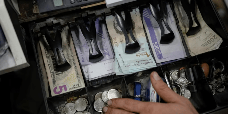 Un vendedor cuenta bolívares venezolanos y billetes de dólares estadounidenses para entregar el cambio a un cliente en un mercado público en Caracas, Venezuela, el martes 18 de enero de 2022.