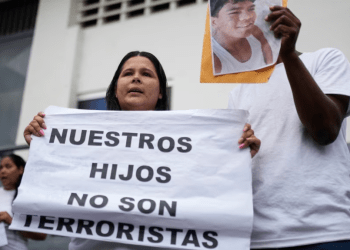 Dionexis García, hermana de Dioner Gómez, cuya fotografía muestra otro miembro de la familia, sostiene un cartel que dice en español "Nuestros hijos no son terroristas" afuera de un centro de detención, donde se encuentran algunos menores en Caracas.